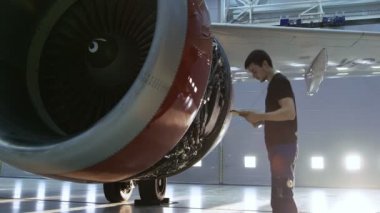 Bir Hangar uçak bakım genç mühendisi olarak / teknisyen / mekanik Tablet bilgisayar ile uçak Jet motoru inceler. O motor kapağı açar ve bir el feneri ile iç inceliyor.