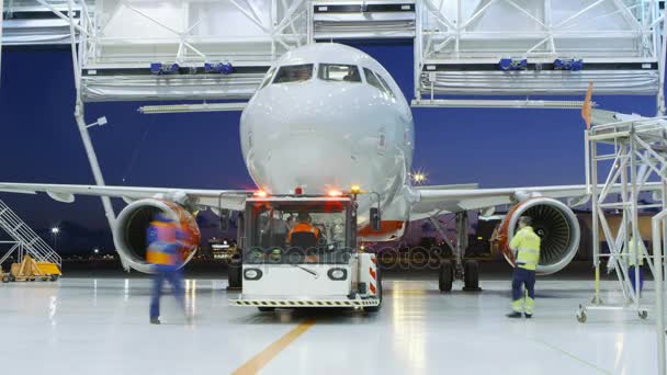 Time-Lapse di un hangar per la manutenzione di un aeromobile in cui un nuovo aeromobile è puntato da un trattore / rimorchiatore di spinta sulla striscia di atterraggio. Equipaggio di meccanici, ingegneri e conducenti Lavori impegnativi . — Video Stock