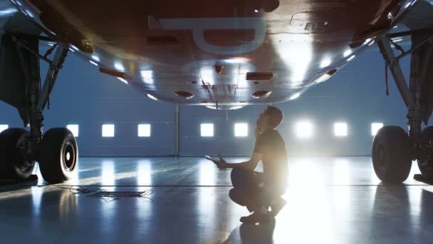 Dans un hangar Entretien des aéronefs Jeune mécanicien / technicien / mécanicien avec ordinateur tablette Inspecte le moteur à réaction de l'avion. Il ouvre la porte du moteur et examine l'intérieur avec une lampe de poche . — Video