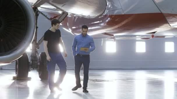 格納庫航空機メンテナンス エンジニア ショー技術データ飛行機技術者にタブレット コンピューター上で。きれいな新品の飛行機と一緒に歩きます。. — ストック動画
