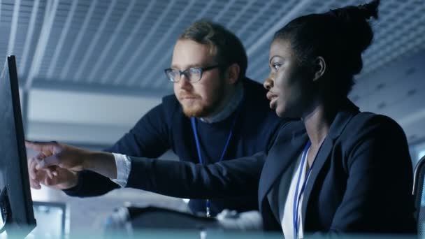 Mujer negra y hombre blanco discuten el trabajo que se muestra en una pantalla de computadora. Trabajan en un brillante y moderno laboratorio / centro de investigación . — Vídeos de Stock