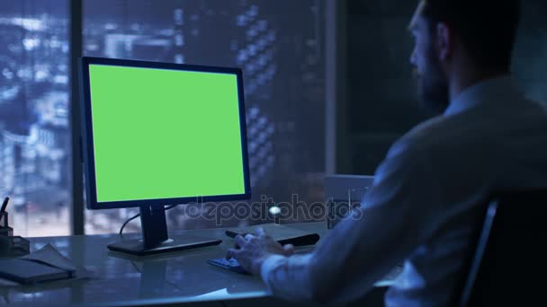 Tarde da noite Empresário trabalha em um computador pessoal com tela de falsificação verde em seu escritório privado com vista para a janela da cidade grande . — Vídeo de Stock