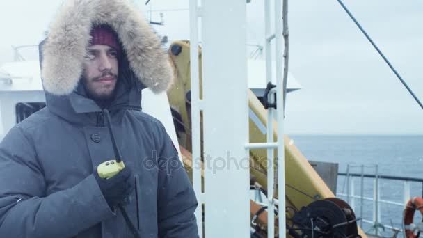 Τυχοδιώκτης σε ζεστό μπουφάν στέκεται στο πλοίο και χρήση ραδιοφώνου για επικοινωνία. Είναι χιονισμένο και θυελλώδη — Αρχείο Βίντεο