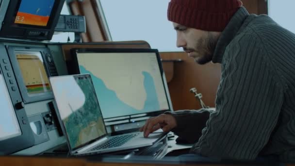 Capitaine de navire de pêche commerciale entouré de moniteurs et d'écrans travaillant avec des cartes marines dans sa cabine . — Video