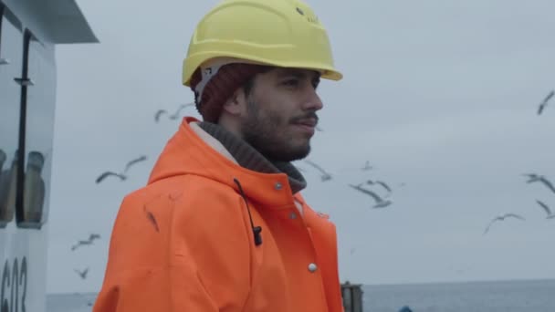 Портрет одетого в яркое защитное пальто улыбающегося рыбака на коммерческой рыбацкой лодке . — стоковое видео