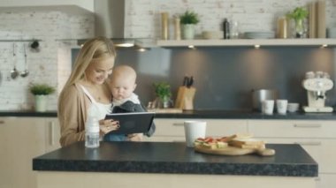 Güzel anne tutan çocuk mutfak onun elinde. İlginç bir şey ekranda gösterir. Bebek belgili tanımlık perde ile etkileşime girer.