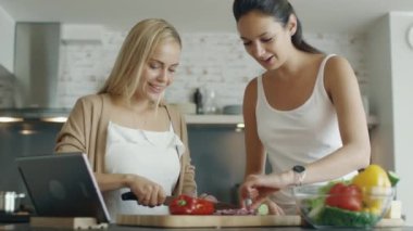 İki genç kız yemek mutfak salata. Onlar da Tablet için arama yemek tarifleri için kullanma 