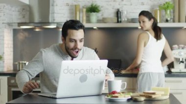 Mutfak önce Laptop genç adam var iyi haber ve aramaları onun kız yemek olan oturma. Her ikisi are gülme ve mutlu.