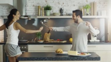 Mutfak genç yakışıklı çift üzerinde eskrim mutfak aletleri ile var. Ocağın üstünde bir şeyler tavada aşçılar.