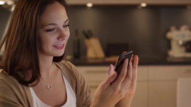 Güzel kız kullanır mutfakta otururken Smartphone. Gülen kız.