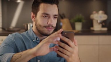 Yakışıklı genç adam gülümseyerek Smartphone mutfakta kullanır..