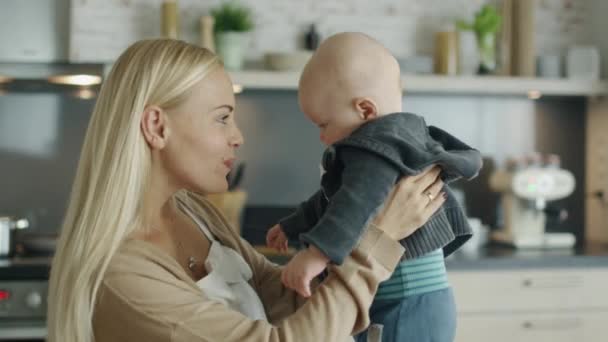 Ung mamma är omvårdnad hennes skrattande barn medan stående på köket. — Stockvideo