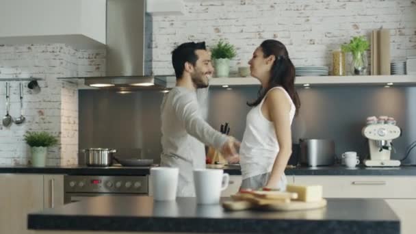 Feliz pareja joven baila en la cocina y luego abrazando . — Vídeo de stock