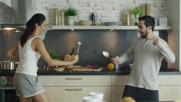 En la cocina joven pareja guapo es esgrima con electrodomésticos de cocina. En la estufa Algo se cocina en la sartén . — Vídeo de stock