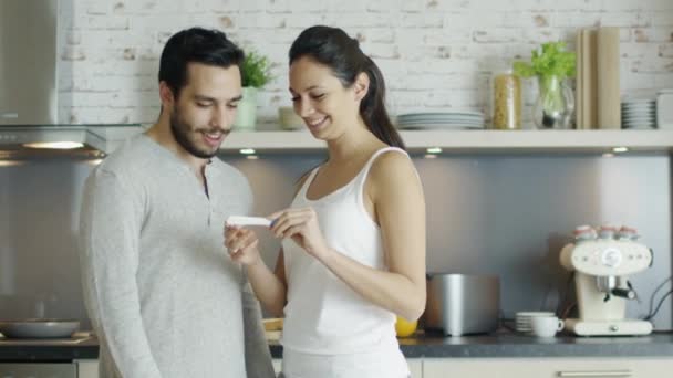 Na kuchnia piękna dziewczyna pokazuje Test ciążowy wynik jej chłopaka i uścisk. Oba są bardzo szczęśliwy. — Wideo stockowe