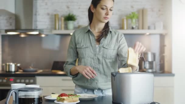 V kuchyni mladá dívka dělá toasty a šíří másla na ně. — Stock video