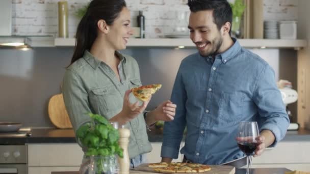 En la cocina joven mujer da su novio mordida de su pizza rebanada . — Vídeo de stock