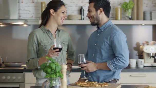 Glückliches Paar teilt Pizza-Scheiben und trinkt Wein in der Küche. — Stockvideo