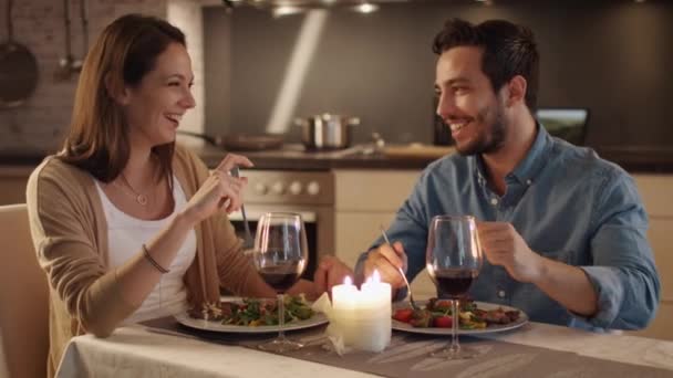 Schönes Paar beim Abendessen bei Kerzenschein in der Küche. Sie essen, trinken und reden. Beide sind gut drauf und lächeln viel. Schlammbewegung. — Stockvideo