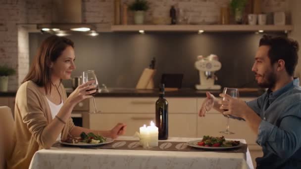 Schönes Paar beim Abendessen bei Kerzenschein in der Küche. Sie trinken Wein, essen und reden. Beide sind gut drauf und lächeln viel. — Stockvideo