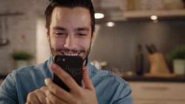Yakışıklı genç adam gülümseyerek Smartphone mutfakta kullanır..