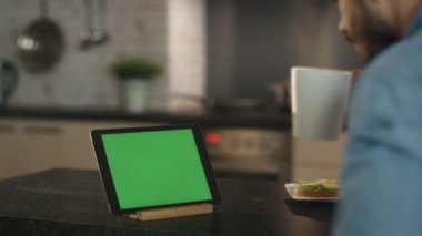 Daha önce yeşil ekran Tablet bilgisayarınızla otururken SIPs bir fincan genç adam.