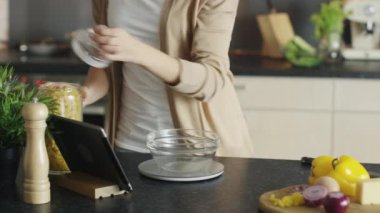 Yakın çekim makarna mutfak ölçekli kase ölçme genç bir kadın. O Tablet bilgisayar tarifi için başvuran.