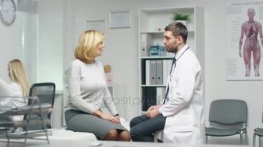 Erkek doktor onun orta yetişkin Bayan hasta danışır. Hemşire Busily bilgisayarın arka planda çalışır..