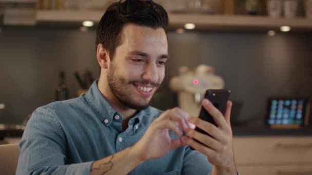 Joven guapo sonriendo utiliza Smartphone en la cocina . — Vídeos de Stock