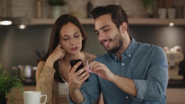 Hermosa pareja joven utiliza Smartphone mientras está sentado en la cocina . — Vídeos de Stock