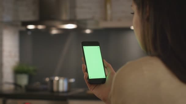 Chica joven sentada en la cocina usando Smartphone con pantalla verde . — Vídeo de stock