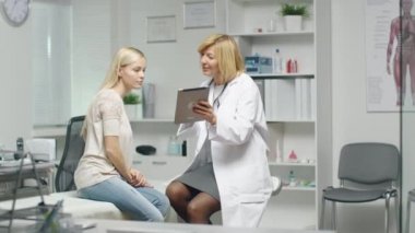 Yetişkin kadın doktor bir şey genç kadın hastasını bir Tablet üzerinde gösterir. Her ikisi de gülümseme ve rahat hissediyorum.