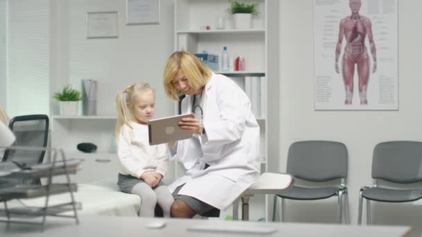 Medico femminile nel suo ufficio mostra Tablet Computer a una bambina paziente . — Video Stock