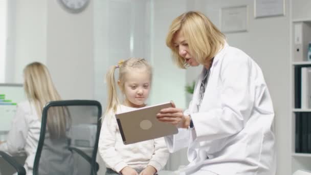 Médico femenino en su oficina muestra Tablet Computer a una pequeña paciente . — Vídeos de Stock