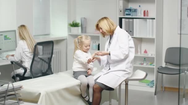 Female Doctor Doing Check Up of a Little Girl's Hands. Nurse Works in the Background. — Stock Video