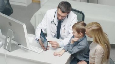 Erkek doktor genç çocuk ve annesi bir Tablet yardımıyla danışır. Onlar gülümseme ve sıcak konuşmak.