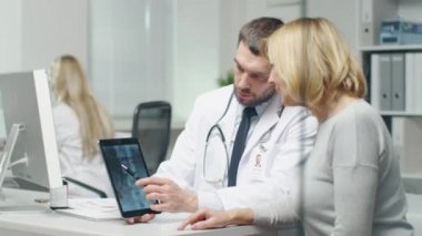 Profesyonel doktor orta yetişkin kadın danışır. O x-ışını görüntüleri Tablet ekranda ona gösterir.