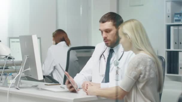 Em Doctor 's Office Professional Doctor Consulta Mulher Bonita Jovem com a Ajuda de um Tablet. Eles olham e a tela e sorriem . — Vídeo de Stock