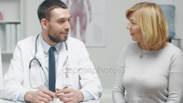 Врач-мужчина консультирует пациентку среднего возраста. Они разговаривают и улыбаются . — стоковое видео