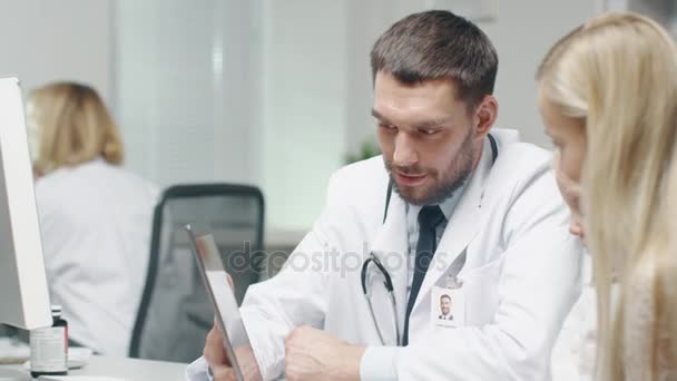 Médico Masculino Consulta Jovem e Sua Mãe com a Ajuda de uma Tablet. Eles sorriem calorosamente . — Vídeo de Stock