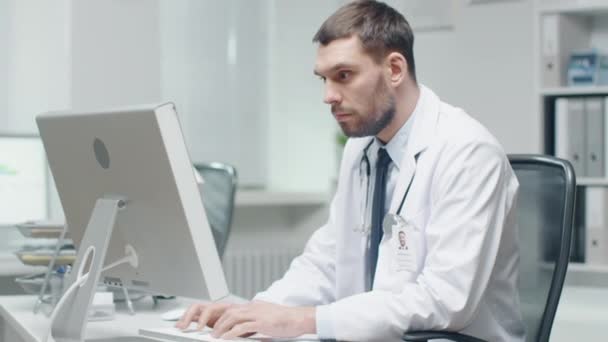 Erkek doktor onun masasında çalışıyor. Kişisel bilgisayar kullanır ve danışır belgeleri. — Stok video