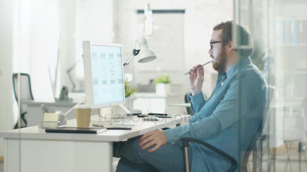 Gericht creatieve Man denkt zittend op zijn werkplek Bureau. Hij bezit potlood en kijkt naar de Desktop computerscherm. — Stockvideo