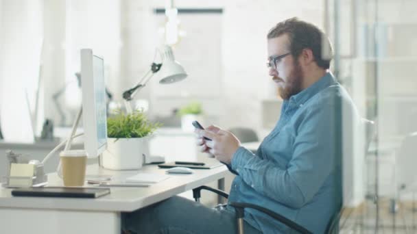 Kreativní člověk používá Smartphone, zatímco sedí na jeho pracovišti. Kancelář je lehký a moderní zelená rostlina na stůl.