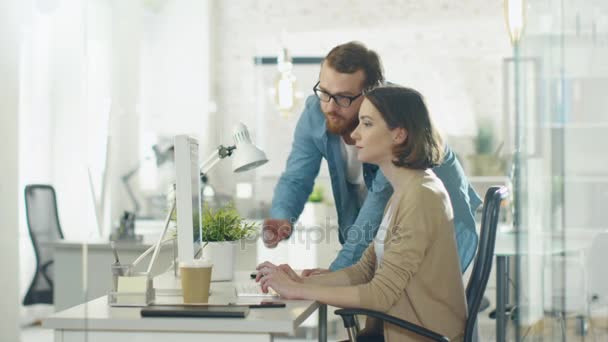 Hombre joven y mujer hermosa discuten temas de trabajo en el lugar de trabajo. Se sienta en la mesa. Él está a su lado. Señala algo en la pantalla . — Vídeo de stock