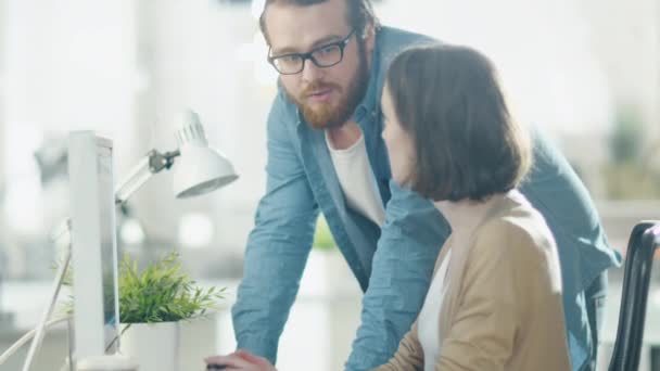 Hombre joven y mujer hermosa discuten temas de trabajo en el lugar de trabajo. Se sienta en la mesa. Él está a su lado. Señala algo en la pantalla . — Vídeo de stock