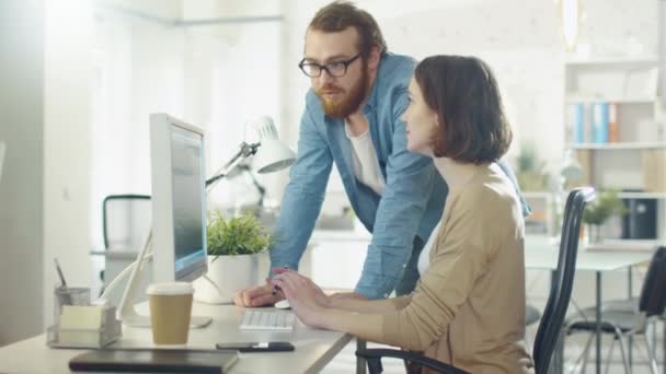 Hombre joven y mujer hermosa discuten temas de trabajo en el lugar de trabajo. Se sienta en la mesa. Él está a su lado. Hablan y señalan algo en la pantalla . — Vídeos de Stock