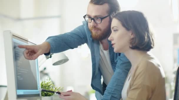 Giovane uomo e bella donna Discutere problemi di lavoro sul posto di lavoro. Si siede a tavola. Sta al suo fianco. Parlano e puntano lo schermo . — Video Stock