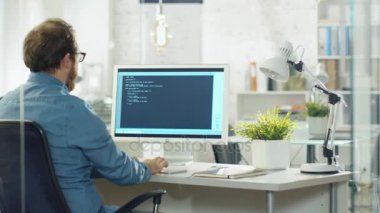Genç geliştirici yazıyor kodu masaüstü bilgisayarında sakallı. O Modern bir ofiste çalışıyor.