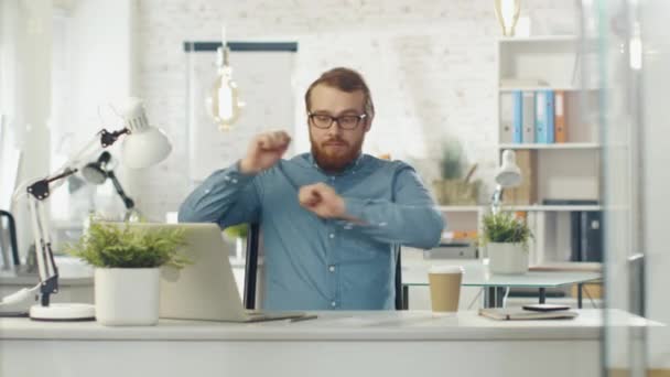 Barbudo tecnología chico comienza a bailar mientras sentado en su escritorio en brillante luz oficina . — Vídeo de stock