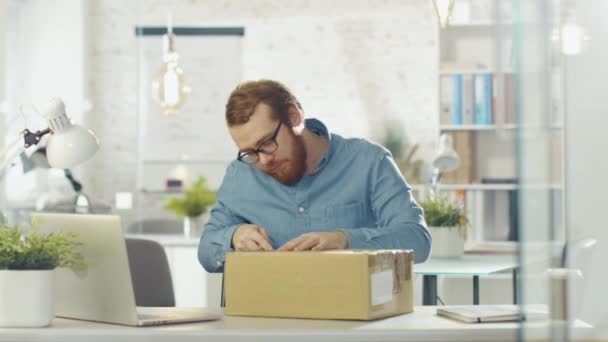 Creative Man Opens Up Parcel While Sitting in His Bright and Modern Office. — Stock Video